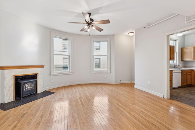 unfurnished living room featuring ceiling fan, sink, a wood stove, and light wood-type flooring