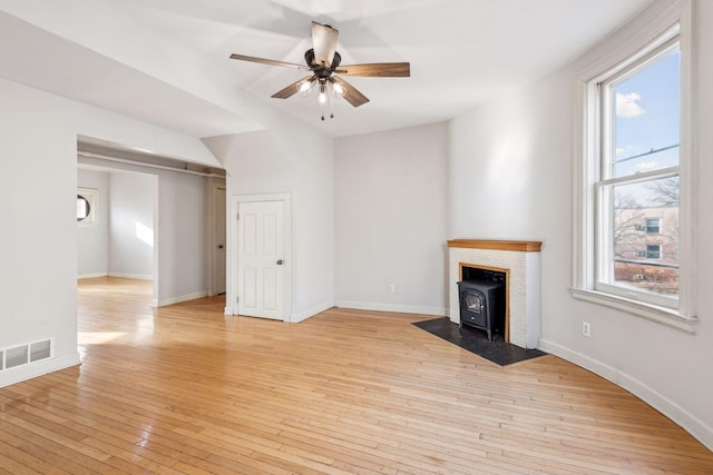 unfurnished living room featuring ceiling fan, a wood stove, and light hardwood / wood-style flooring