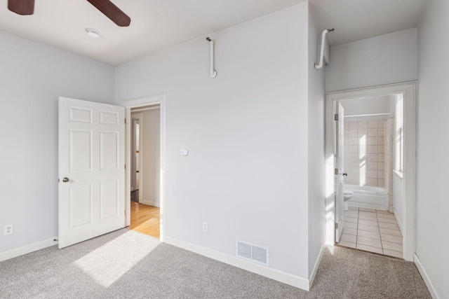 unfurnished bedroom with ensuite bathroom, light colored carpet, and ceiling fan