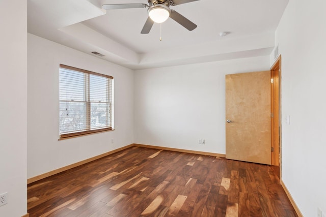 empty room with a tray ceiling, dark hardwood / wood-style floors, and ceiling fan