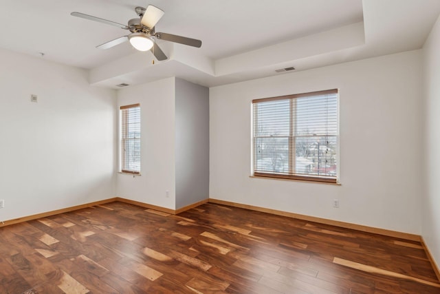 empty room featuring plenty of natural light, dark hardwood / wood-style floors, ceiling fan, and a tray ceiling