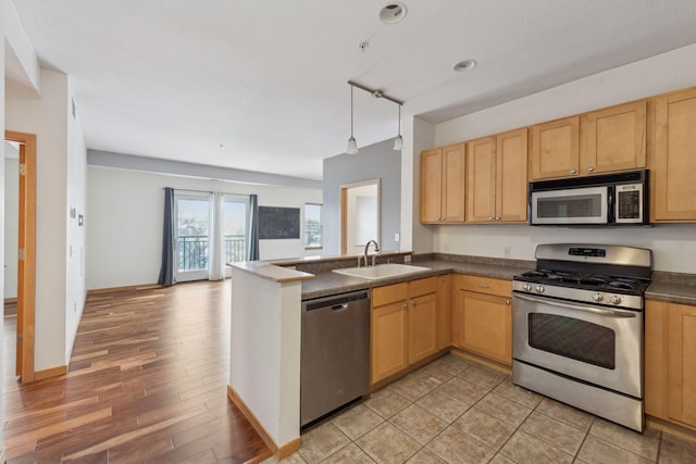 kitchen with appliances with stainless steel finishes, sink, hanging light fixtures, kitchen peninsula, and light hardwood / wood-style flooring