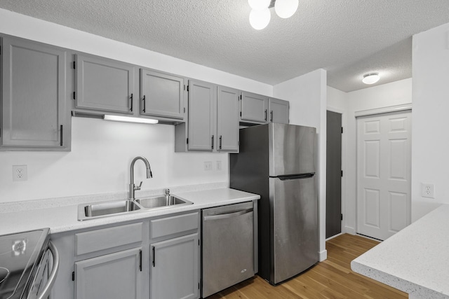 kitchen with appliances with stainless steel finishes, a textured ceiling, gray cabinetry, sink, and light hardwood / wood-style flooring