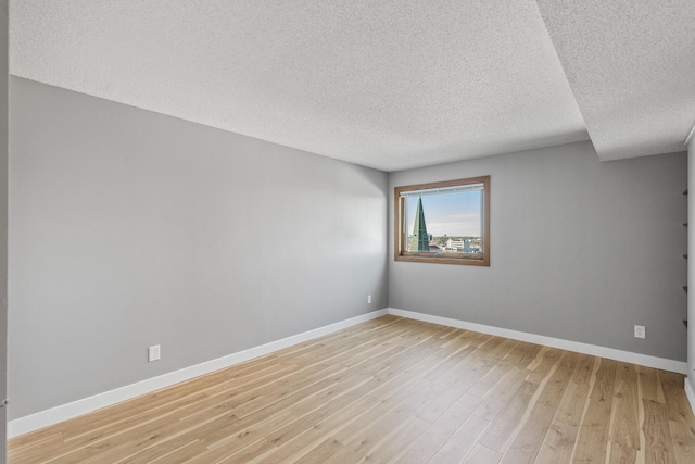 empty room featuring light wood-style floors, baseboards, and a textured ceiling