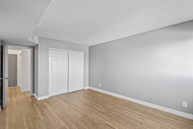 unfurnished bedroom with light wood-style floors, a closet, baseboards, and a textured ceiling