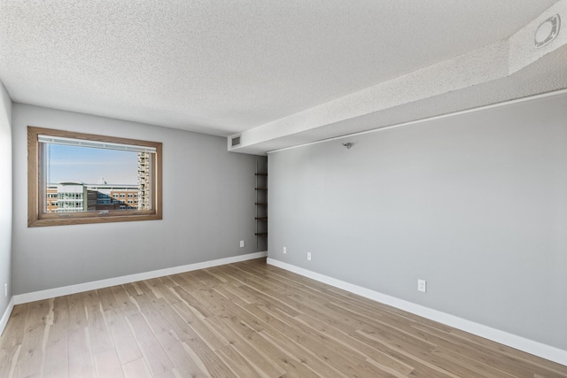 spare room with light wood-type flooring, visible vents, a textured ceiling, and baseboards