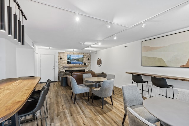 dining room with light wood finished floors, rail lighting, and a stone fireplace