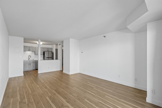 unfurnished living room with baseboards, a sink, and light wood-style floors