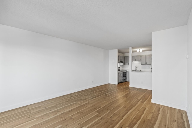 unfurnished living room with light wood-type flooring, baseboards, and a textured ceiling