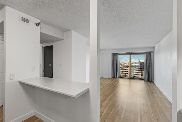 kitchen featuring a textured ceiling, wood finished floors, visible vents, and baseboards