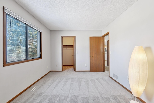 unfurnished bedroom with a walk in closet, light colored carpet, a textured ceiling, and a closet