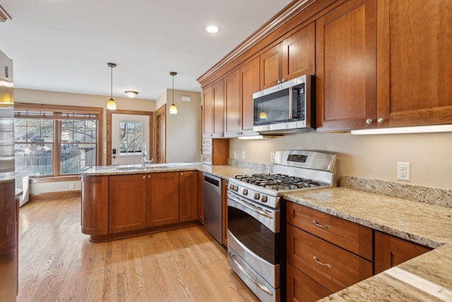 kitchen with stainless steel appliances, pendant lighting, light stone counters, and light hardwood / wood-style flooring