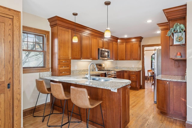 kitchen with sink, decorative light fixtures, appliances with stainless steel finishes, kitchen peninsula, and light stone countertops