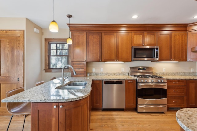 kitchen featuring pendant lighting, sink, a kitchen bar, stainless steel appliances, and light stone countertops