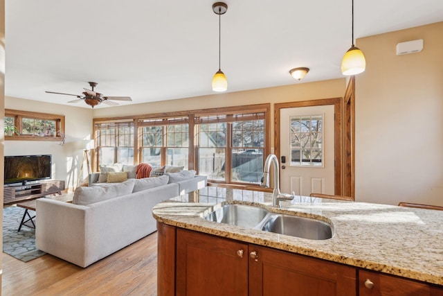 kitchen featuring sink, decorative light fixtures, light wood-type flooring, ceiling fan, and light stone countertops