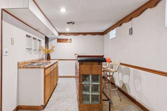 kitchen with a kitchen breakfast bar, cooktop, light colored carpet, and a textured ceiling