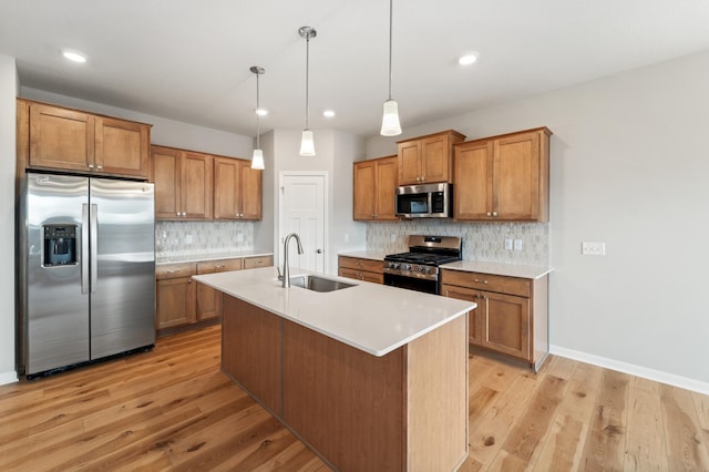 kitchen with sink, a kitchen island with sink, stainless steel appliances, decorative backsplash, and decorative light fixtures