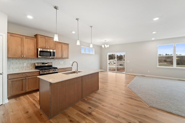 kitchen with appliances with stainless steel finishes, sink, backsplash, hanging light fixtures, and a kitchen island with sink