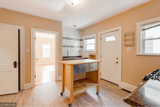 kitchen with pendant lighting, sink, light wood-type flooring, a textured ceiling, and gas range oven