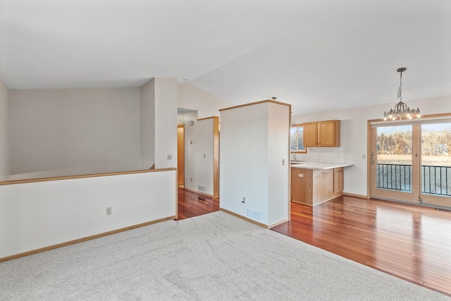 unfurnished living room featuring an inviting chandelier, lofted ceiling, and light hardwood / wood-style flooring