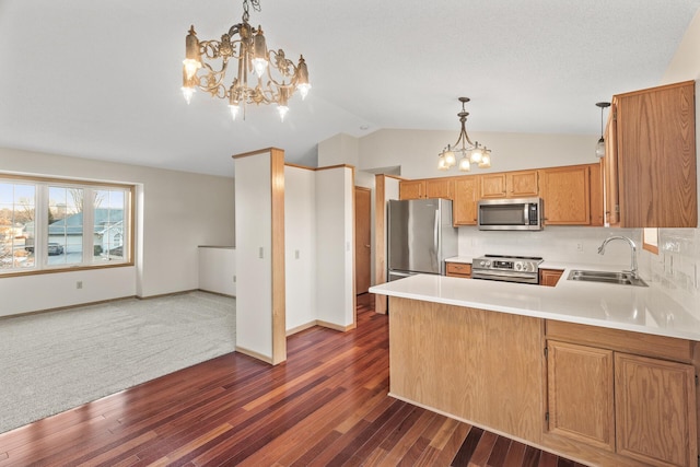 kitchen featuring sink, appliances with stainless steel finishes, hanging light fixtures, vaulted ceiling, and kitchen peninsula