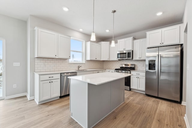 kitchen with a kitchen island, appliances with stainless steel finishes, decorative light fixtures, white cabinetry, and backsplash