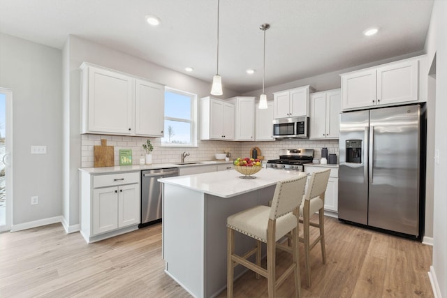 kitchen with tasteful backsplash, white cabinets, stainless steel appliances, light countertops, and light wood-type flooring