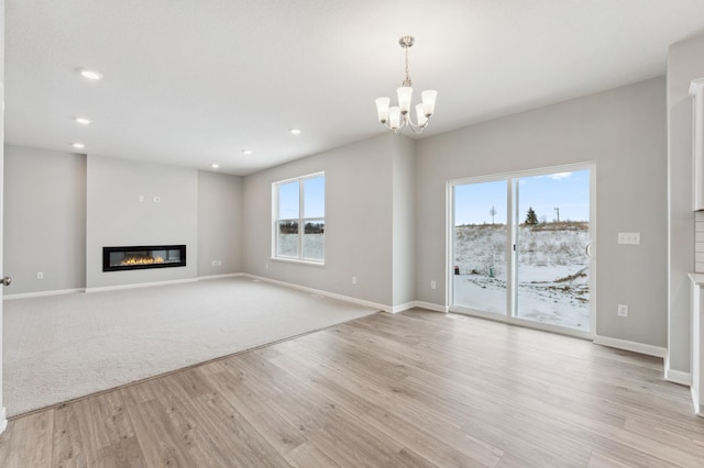 unfurnished living room featuring light wood finished floors, recessed lighting, baseboards, and a glass covered fireplace