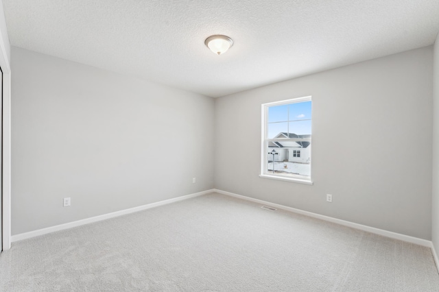 empty room featuring carpet, visible vents, a textured ceiling, and baseboards