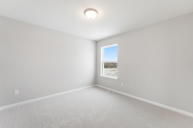 empty room featuring carpet floors, visible vents, a textured ceiling, and baseboards