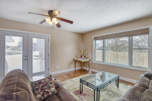 living area with french doors, ceiling fan, a textured ceiling, wood finished floors, and baseboards