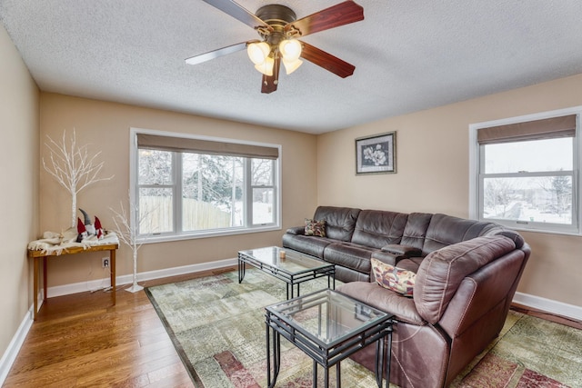 living room featuring a ceiling fan, a textured ceiling, baseboards, and wood finished floors