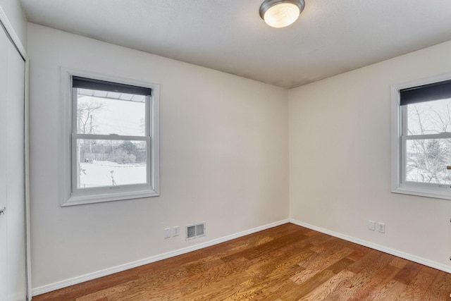 empty room featuring a wealth of natural light, baseboards, visible vents, and wood finished floors