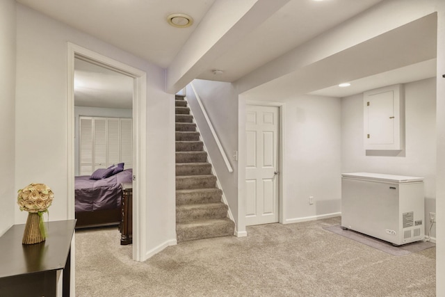 finished below grade area with light carpet, electric panel, baseboards, stairway, and fridge