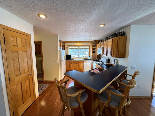 kitchen featuring washer / dryer, a kitchen breakfast bar, dark hardwood / wood-style floors, kitchen peninsula, and white appliances