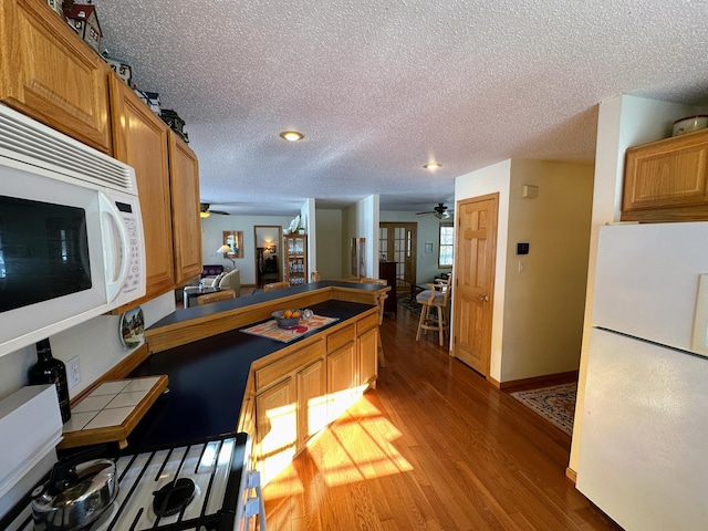 kitchen with white appliances, kitchen peninsula, hardwood / wood-style floors, and a textured ceiling