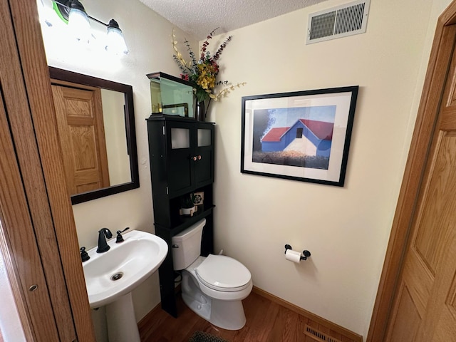 bathroom with hardwood / wood-style floors, sink, toilet, and a textured ceiling