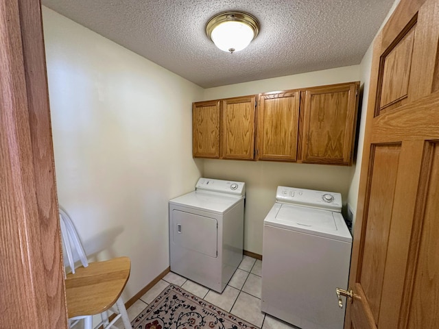 clothes washing area with light tile patterned flooring, cabinets, washer and dryer, and a textured ceiling