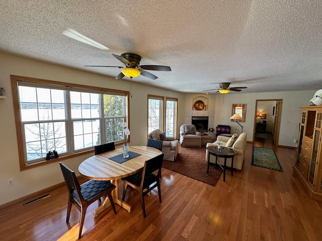 dining room featuring ceiling fan, wood-type flooring, a tile fireplace, and a textured ceiling