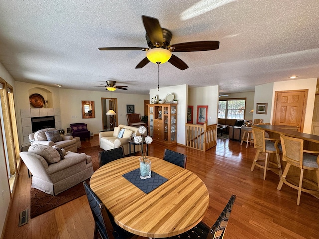 dining room with a tiled fireplace, hardwood / wood-style floors, and a textured ceiling