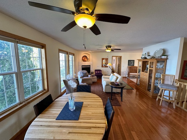 43561 Paul Lake Dr, Edna Twp, MN 56573 - dining space with wood finished floors, a tiled fireplace, a textured ceiling, and a ceiling fan