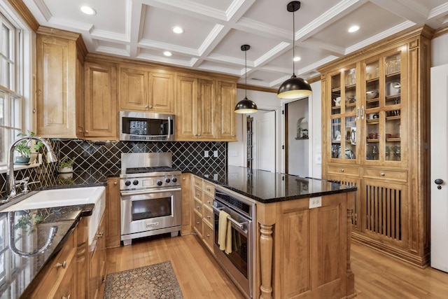 kitchen featuring sink, hanging light fixtures, dark stone countertops, appliances with stainless steel finishes, and light hardwood / wood-style floors