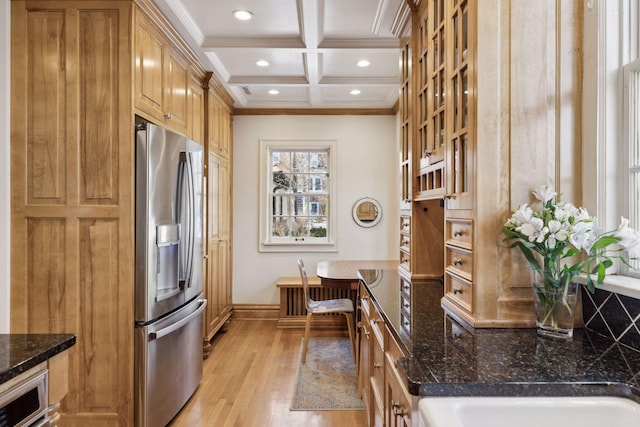 kitchen with coffered ceiling, stainless steel fridge with ice dispenser, ornamental molding, dark stone counters, and light hardwood / wood-style floors