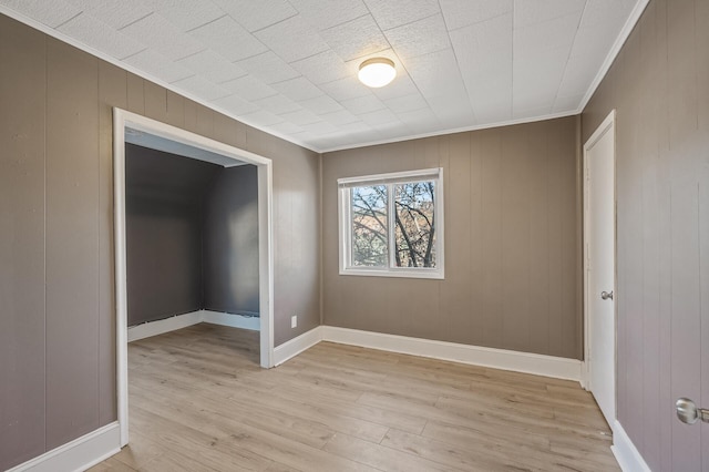 unfurnished room with ornamental molding, wooden walls, and light wood-type flooring