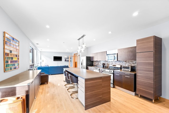 kitchen with decorative light fixtures, backsplash, a kitchen island, a kitchen bar, and appliances with stainless steel finishes