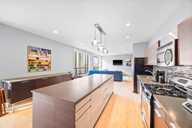 kitchen with a center island, decorative backsplash, hanging light fixtures, light wood-type flooring, and appliances with stainless steel finishes