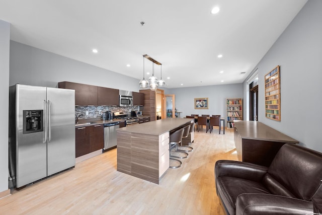 kitchen with a kitchen island, a kitchen bar, decorative backsplash, dark brown cabinetry, and stainless steel appliances