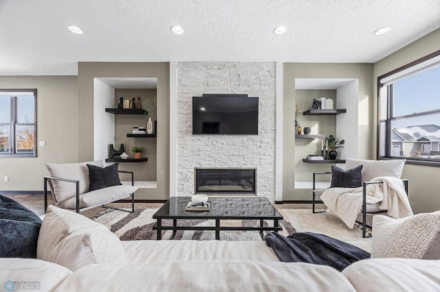living area featuring a stone fireplace, a textured ceiling, baseboards, recessed lighting, and built in features