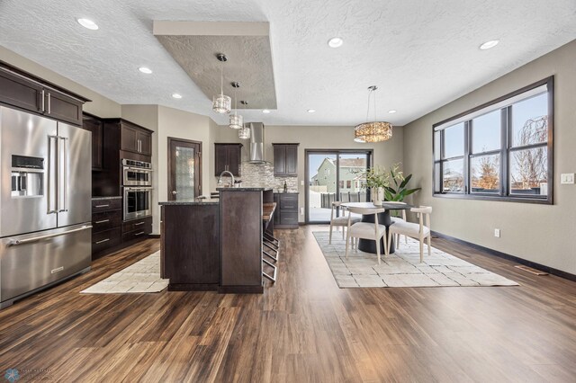 kitchen with appliances with stainless steel finishes, a textured ceiling, dark wood-style floors, backsplash, and dark brown cabinetry