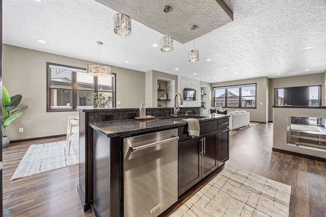 kitchen featuring stainless steel dishwasher, a sink, wood finished floors, a textured ceiling, and open floor plan